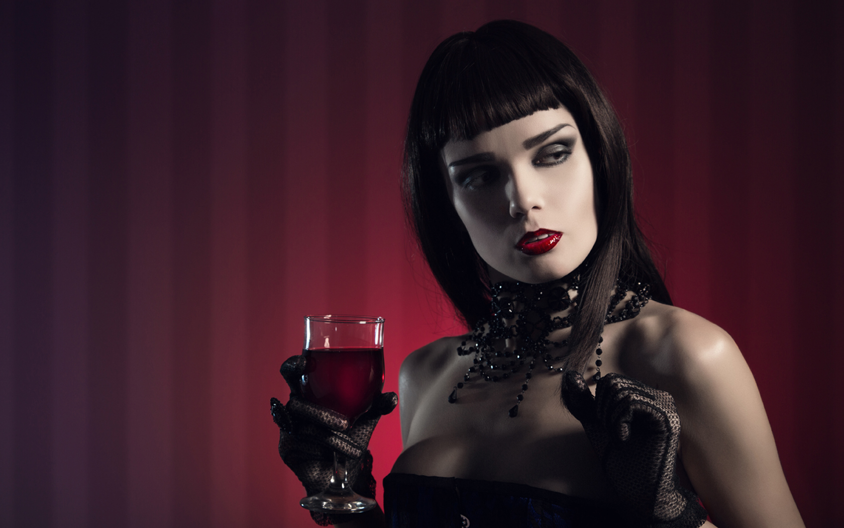 attraktive Frau mit schwarzen Haaren im Abendkleid in linker Hand ein Glas Rotwein